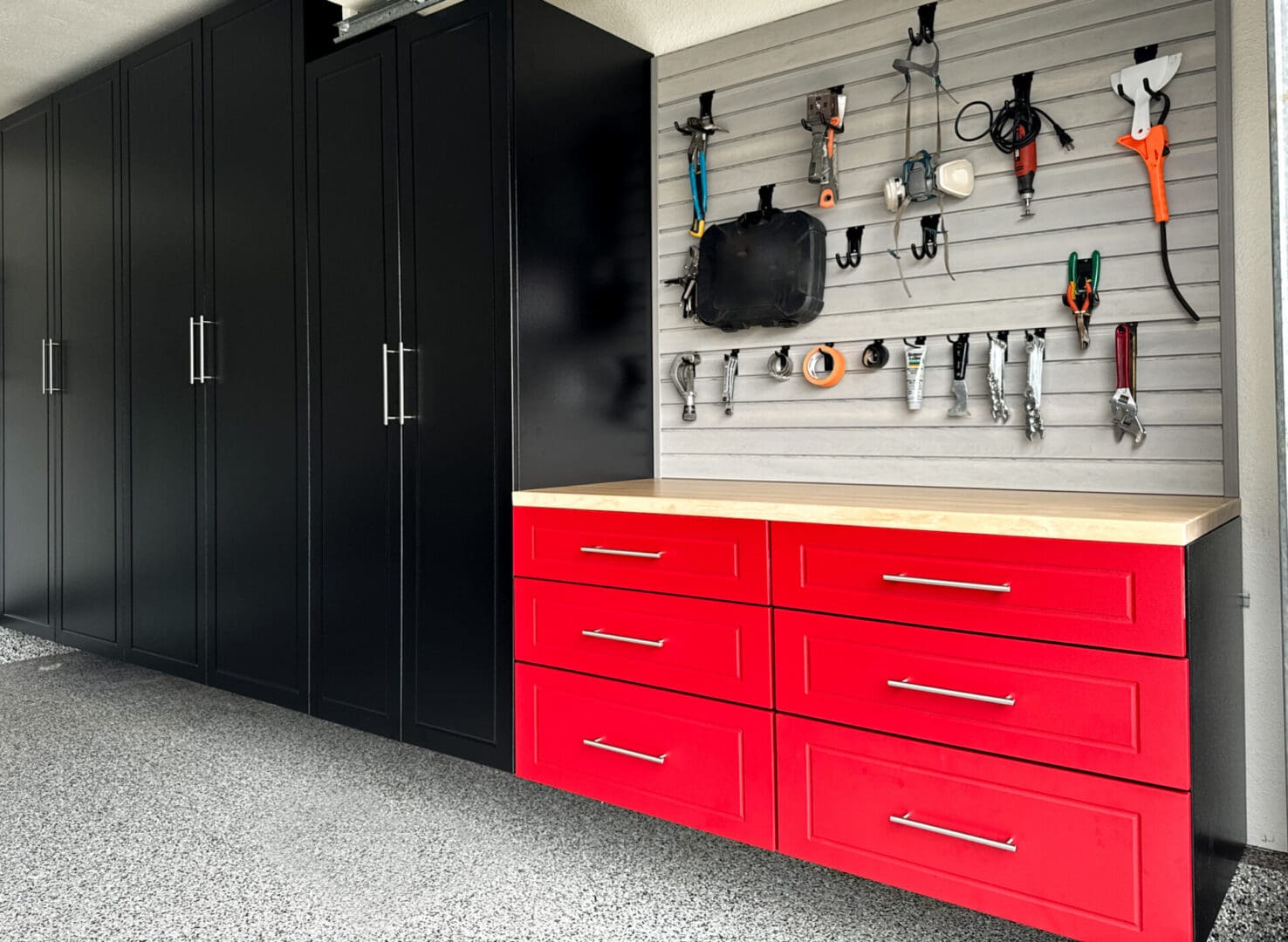 A red and black garage with cabinets, drawers and hooks.